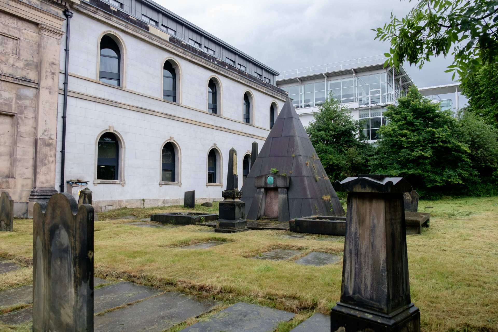 Looking at the pyramid-shaped tomb in the centre of the graveyard. There are other, smaller, more traditionally shaped graves around it. To the left of the photo is the rebuilt St Andrews building