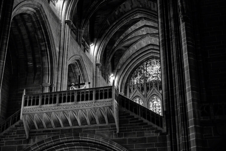 looking up at the back of the cathedral. part of a large stained glass window is at the back. in the foreground is a bridge-like structure with a cross on it