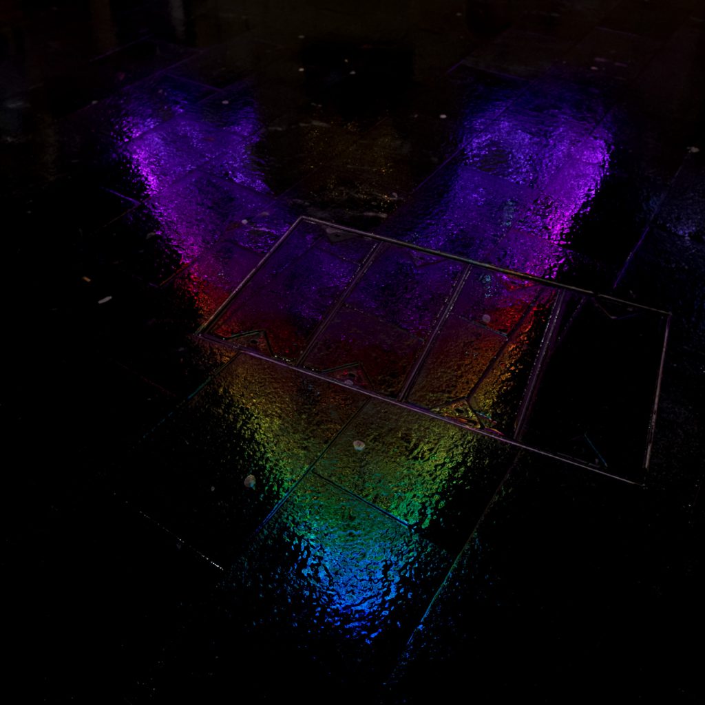 A reflection of the colourful Christmas tree on the wet pavement