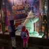 The two girls standing in front of a shop window with a pole-dancing polar bear