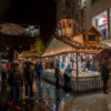 A German-style Christmas market stall with pick-and-mix sweets on a pedestrianised part of town. There are lots of shoppers walking up and down, some with umbrellas up