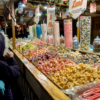 One of the girls standing in front of the pick-and-mix market stall, looking at large piles of flavoured (and brightly coloured) fudges