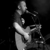 A man on stage playing a guitar and singing into a microphone