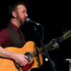 A man playing a guitar and singing into a microphone