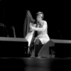 A woman on stage playing a medium-sized harp