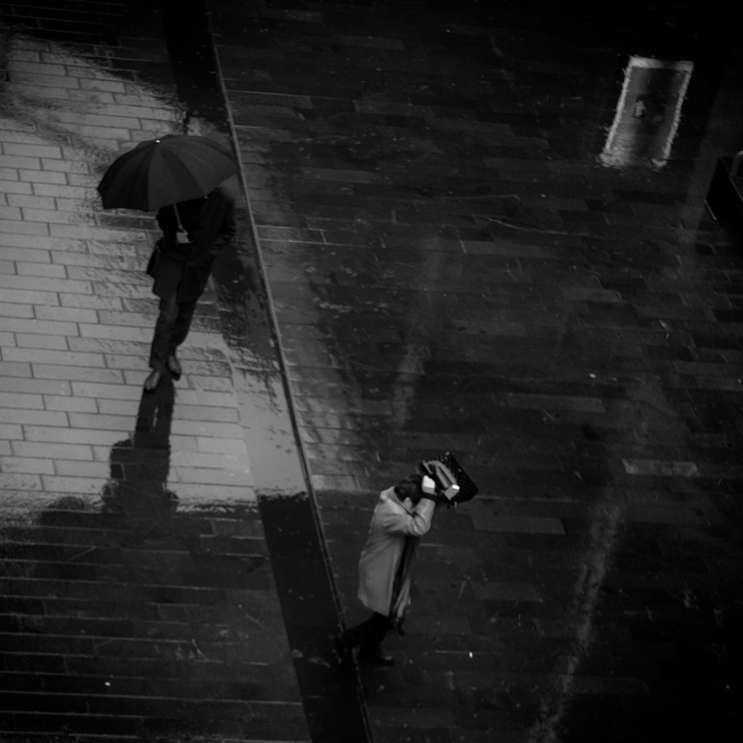 Two people walking through the rain. One has an umbrella while the other is holding her bag over her head and is rushing to get out of the rain