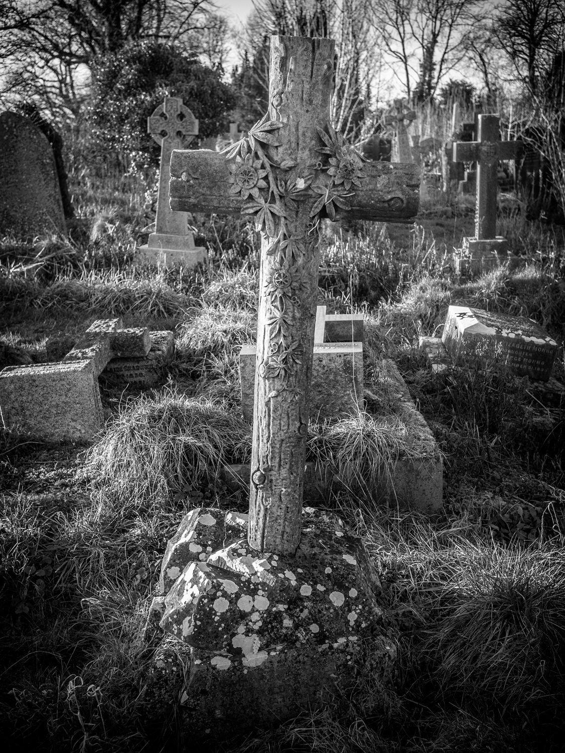 A stone cross carved to look like it's made of wood. It also has carved stone flowers draping around the cross