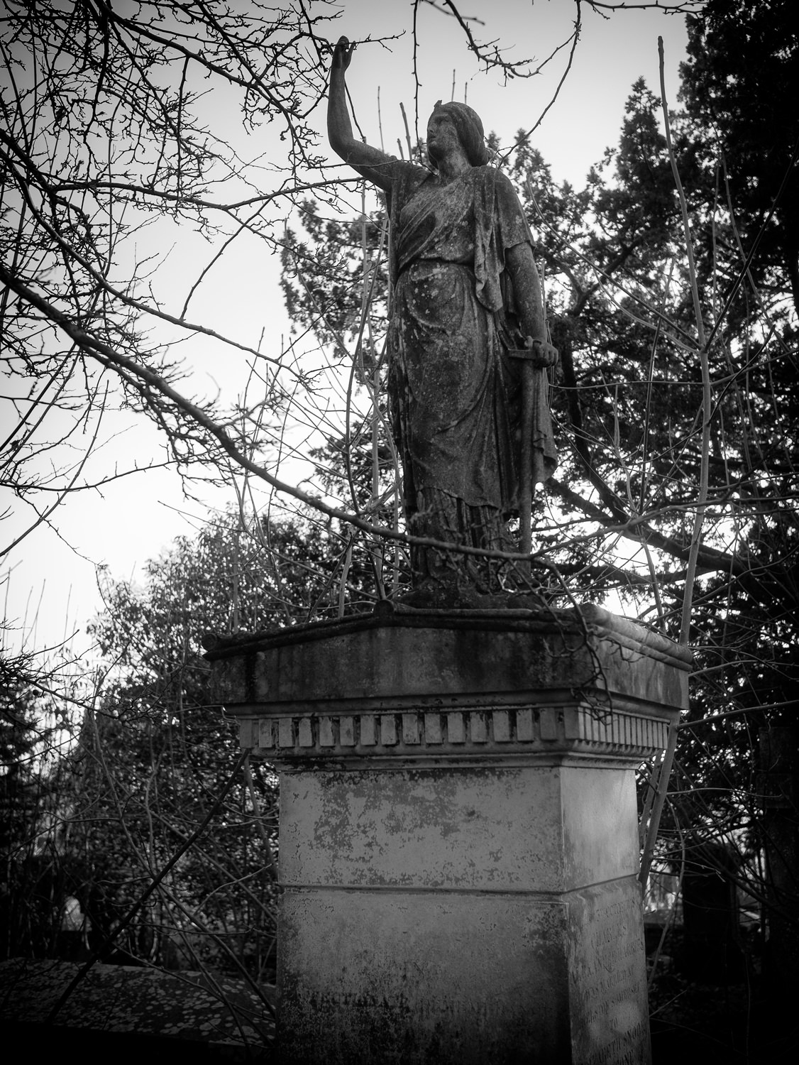 A statue in a typically Victorian, neo-classical style. The statue is a woman in draped clothes, with one arm up in the air.