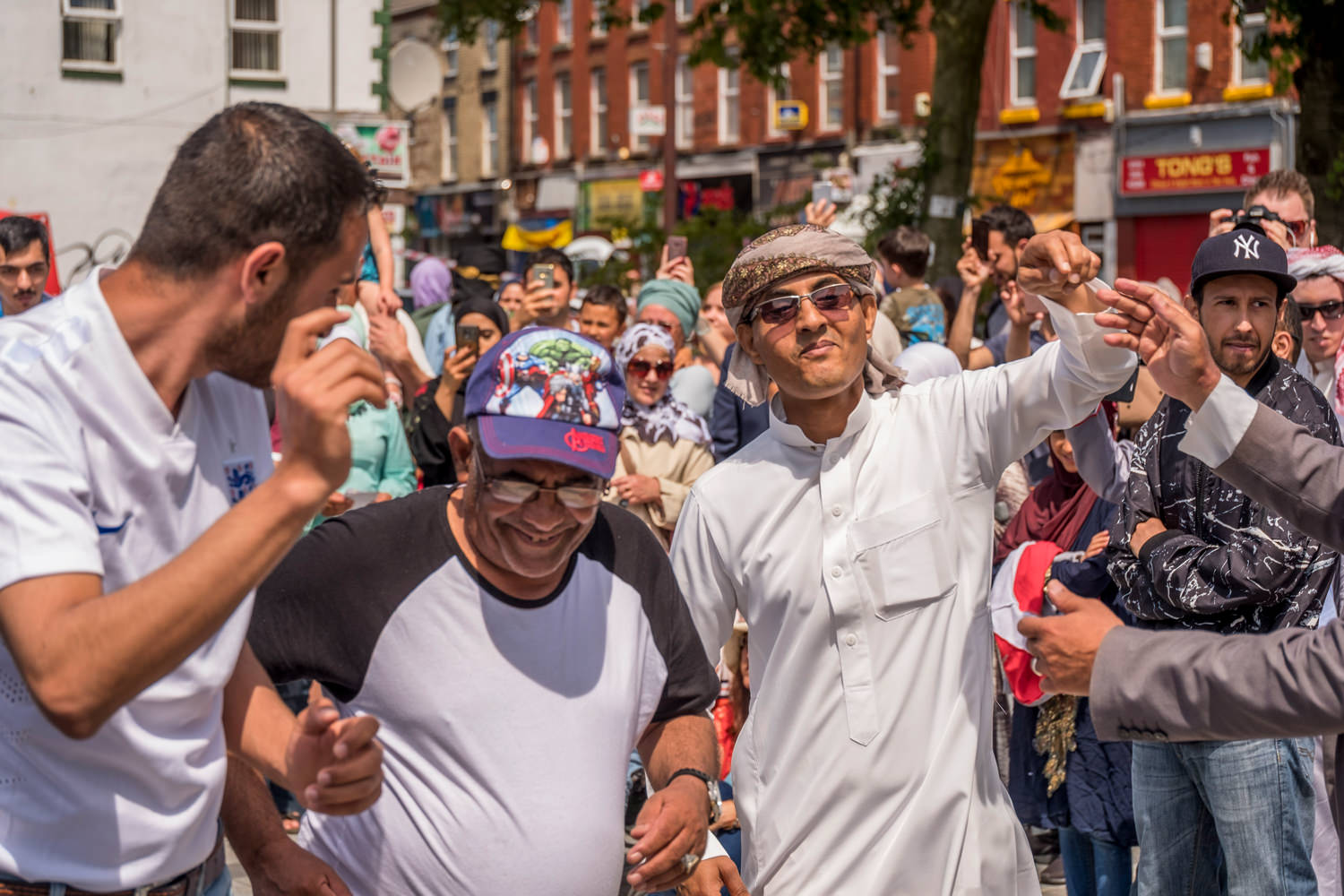 A crowd of people. Three men, one in traditional Arab clothes, are dancing and smiling.