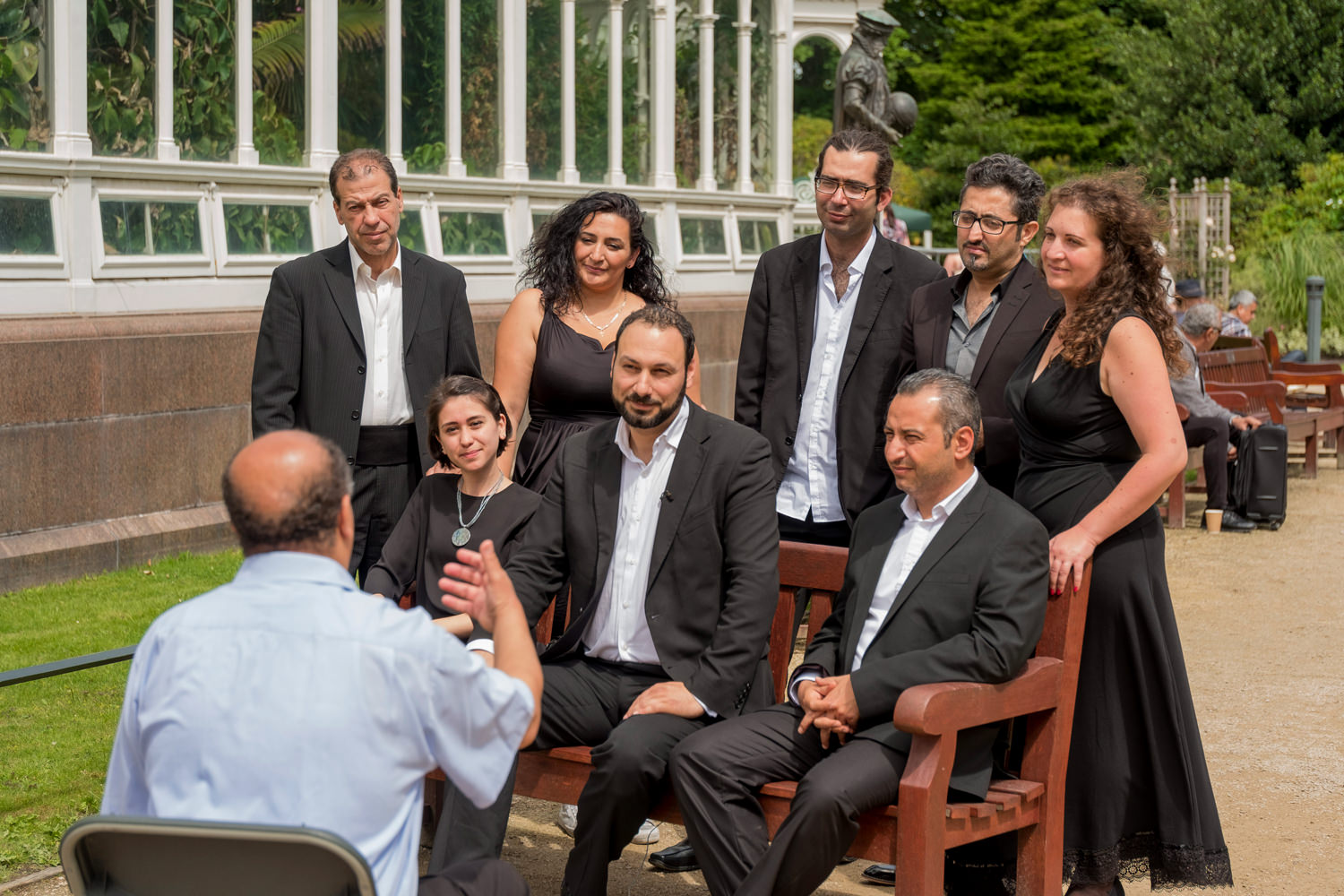 A group of men and women in smart, black clothes with a man sitting on a chair talking to them.