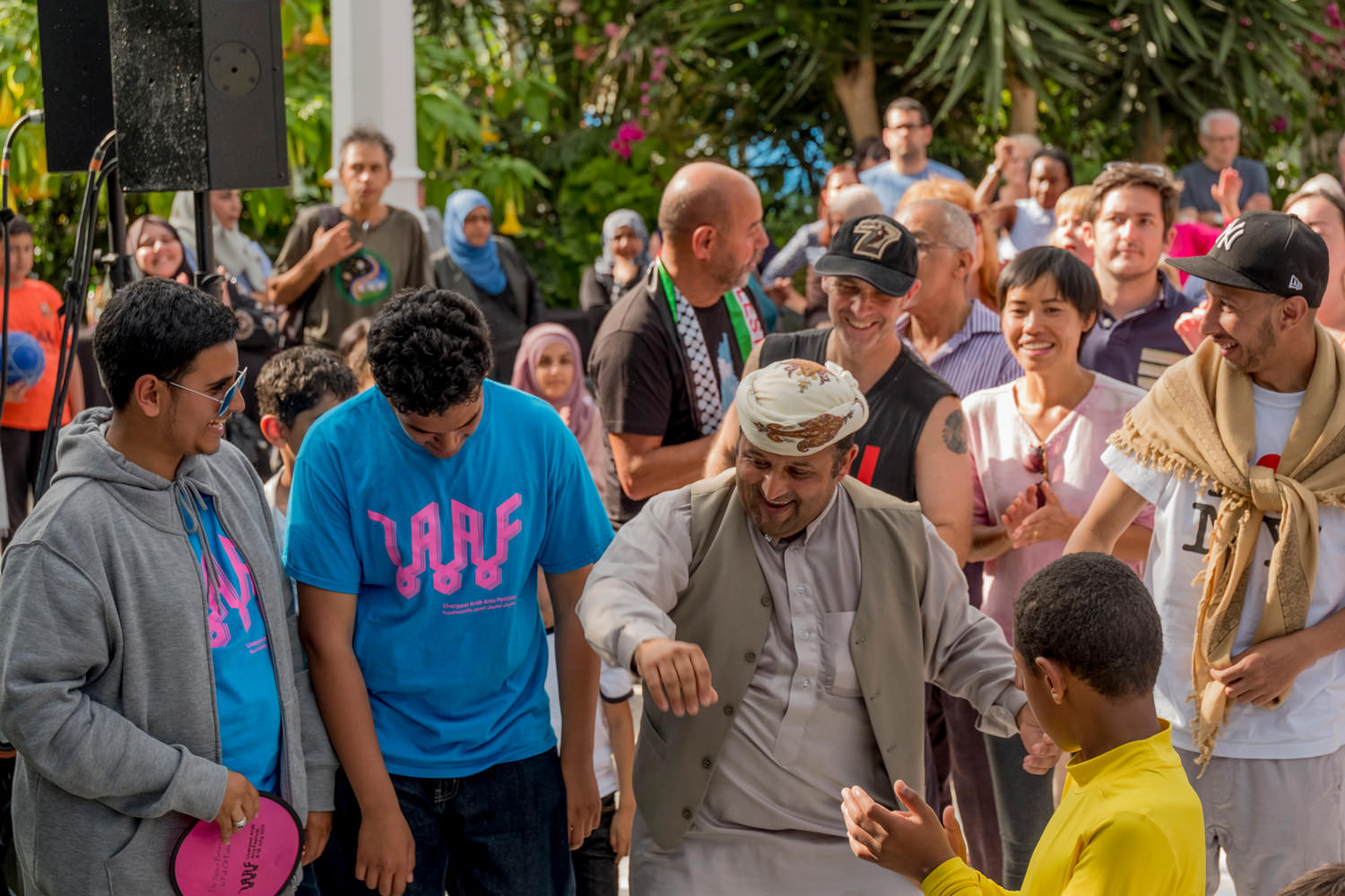 A group of men and teen boys dancing. People are laughing and smiling.