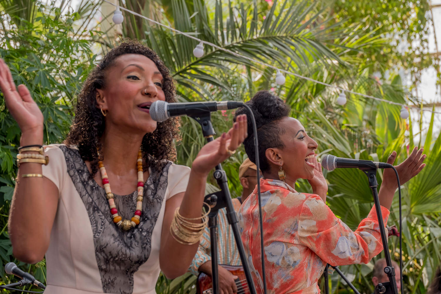 Two women standing next to each other, singing. They're clapping their hands and smiling as they sing.