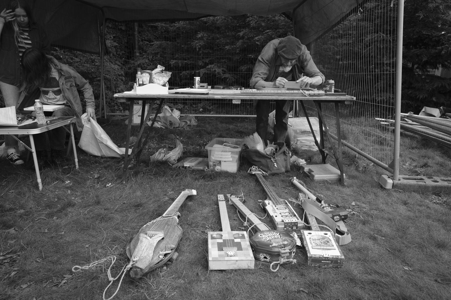 Dennis working at his table with six handmade ukuleles on the grass in front of him.