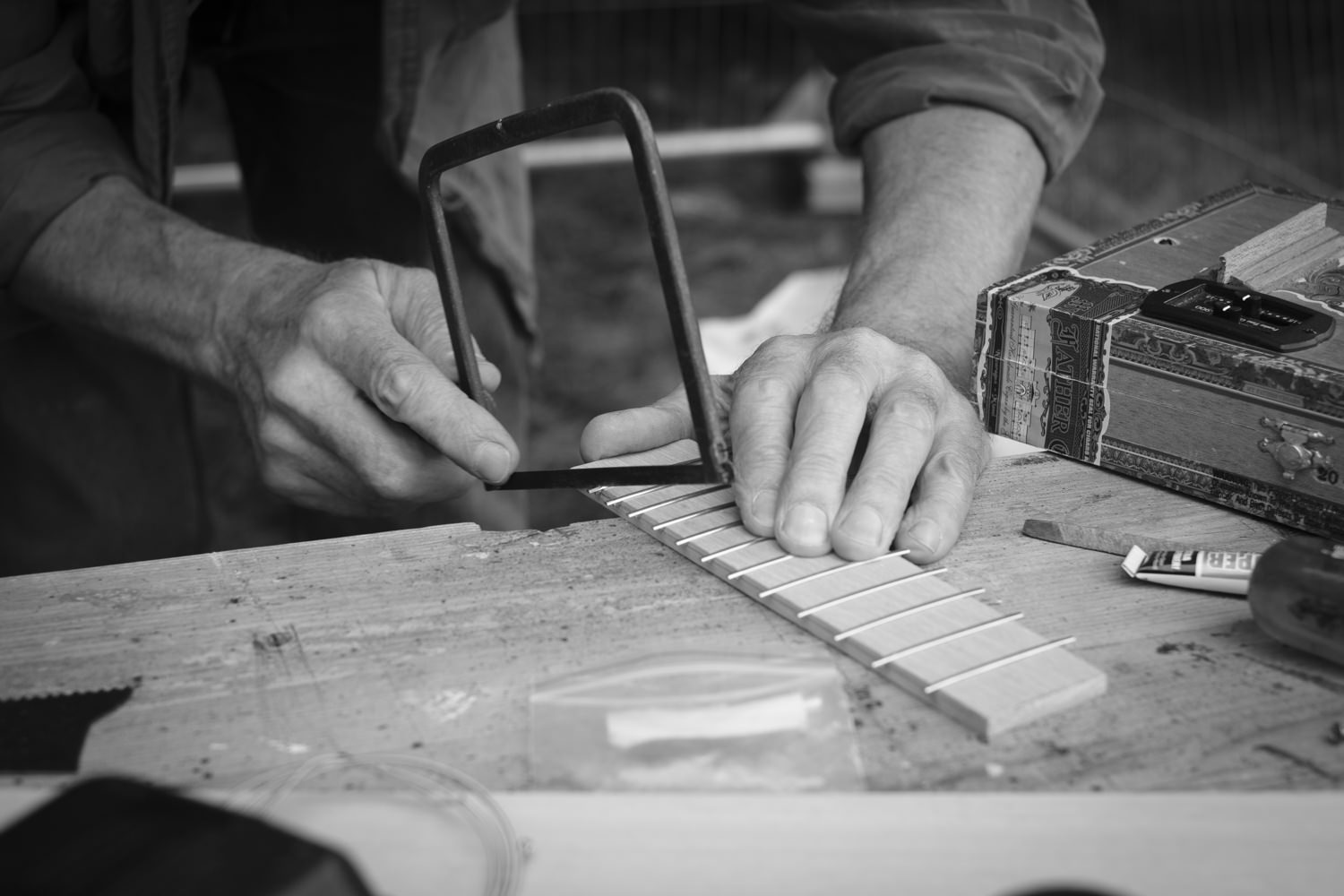 A closeup of Dennis' hands using a small hacksaw to remove excess metal from frets on a fretboard.