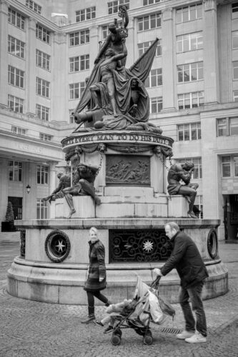 a man and woman with their pushchair walking past a statue