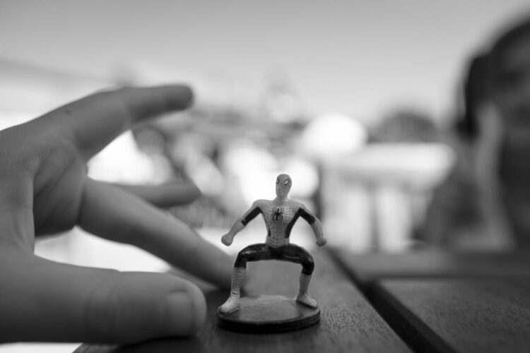 A hand holding a plastic spiderman toy on a table