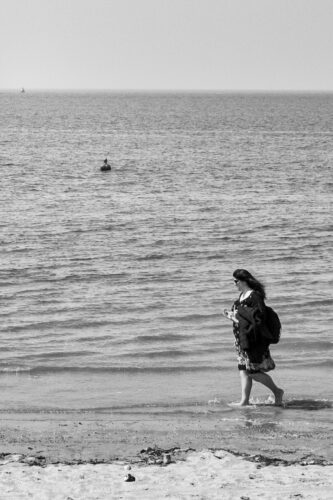 a woman walking along the edge of the sea on a beach