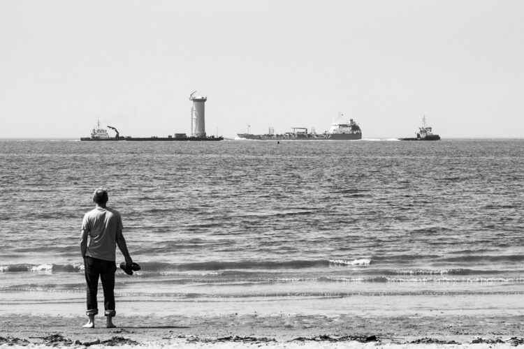 a man standing by the sea edge watching ships